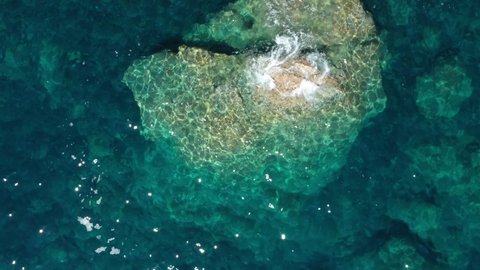 Ocean waves movement on stones top view. Slow flight over large rocks in the ocean. Aerial view of clear water in the sea. Large stones in the transparent clean water of the ocean Drone video.