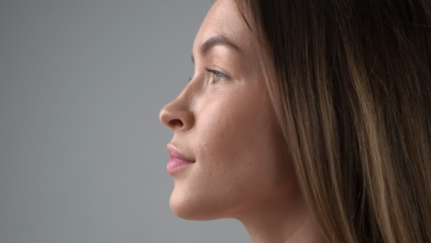 Beauty face of a young blonde woman in profile close-up. Smile, beautiful eyes, lips and teeth. Grey background
