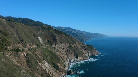 Aerial over the Pacific Ocean with a small highway cutting through the mountainside.