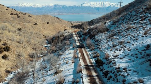 A truck driving on a dirt road through a narrow canyon towards a valley with a lake and snow-capped mountains