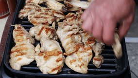 A male hand in close-up turns a chicken meat on an electric grill. The recipe for chicken meat and wings. Cooking with an electric grill without oil.  Outdoor picnic in the garden.