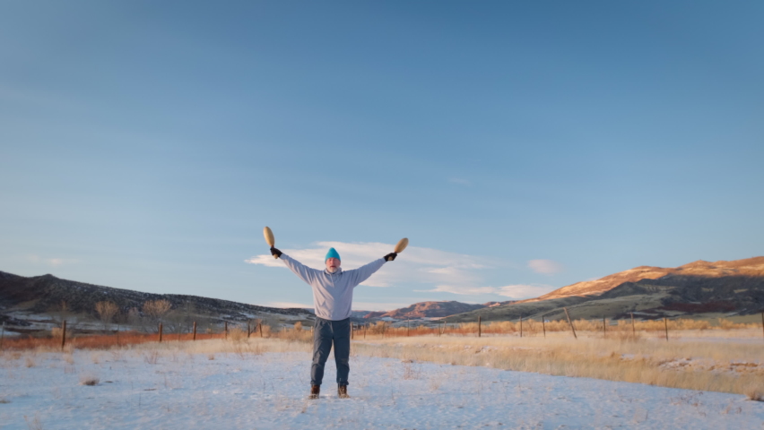 senior man is exercising outdoor with wooden Indian clubs, winter scenery at Colorado foothills