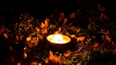 Grave candle light in autumn leaves on the ground, glittering, flame in strong wind disperse the darkness of the night.
