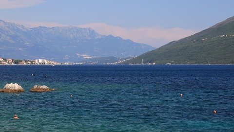 Clear water splashes into sea on  summer beach against  high mountains in Herceg Novi, Montenegro. Recreation and tourism in the Bay of Kotor, Mediterranean Sea in Montenegro