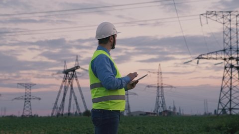 Silhouette of an electrical engineer in hard hat at sunset with tablet. business technology industry. concept electrical voltage tower towers. high voltage substation with distribution cables. energy