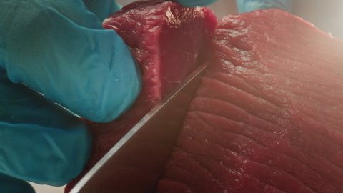 A man cook cuts a fresh red raw fillet in a butcher's shop with a kitchen knife. Slices Premium ribeye meat or marbled beef. Steak production for restaurants, slaughterhouse, meat industry. macro shot