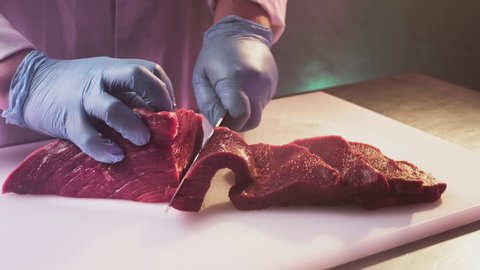 A man cook cuts a fresh red raw fillet in a butcher's shop with a kitchen knife. Slices Premium ribeye meat or marbled beef. Steak production for restaurants, slaughterhouse, meat industry. Wagyu