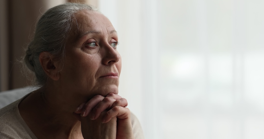 Close up of sad pensive 70s retiree woman put chin on folded palms experiences sentimental longing for period in past looks into distance, sit indoor. Melancholy, retired life, nostalgic mood concept Royalty-Free Stock Footage #1087284989