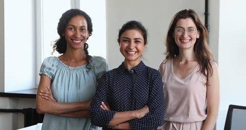 Three millennial multiethnic businesswomen staff members pose at workplace smile look at camera. Group of friendly confident company employees, quality services, career advance and partnership concept