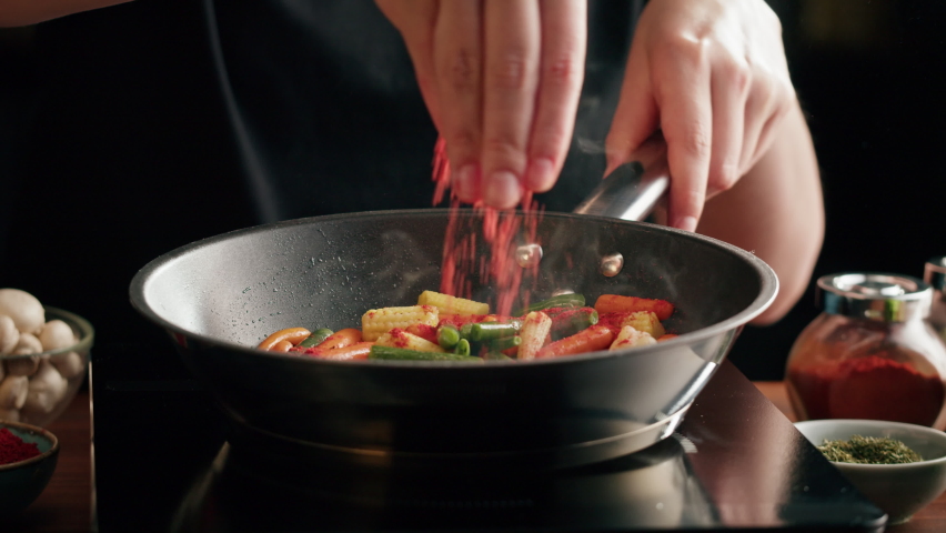 Chef frying vegetables in pan close-up. Woman chief cooking dish with grilled asparagus, corn and carrots, vegetarian food. Spicy arabian and mexican cuisine.