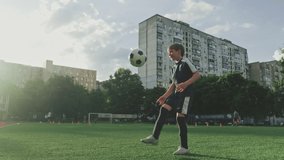 SLOW MOTION - Boy trains professionally on a football field with a ball. Training with a ball on football pitch while sunset. Active child makes a feint with football on a green field. Sport concept