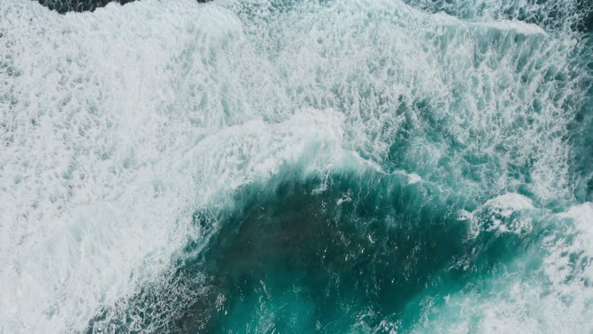 Zoom in on the big power ocean waves with white wash. Aerial top view footage of fabulous sea tide on a stormy day. Drone filming breaking surf with foam in the Indian ocean. Big swell in Bali. Royalty-Free Stock Footage #1087293806
