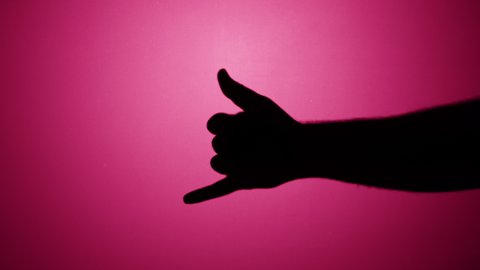 Shadow of Hawaiian shaka greeting gesture isolated on pink neon background. Showing hand gesturing with fingers close-up.