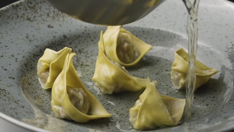 Chinese wonton dumplings are filled with broth. Stuffed steam dumplings dim sum in a gray plate revolve close up. Asian traditional soup with wontons, stuffed with meat. Restaurant. Slow motion.