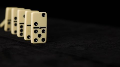 Close up falling white dominoes, domino effect on black background.