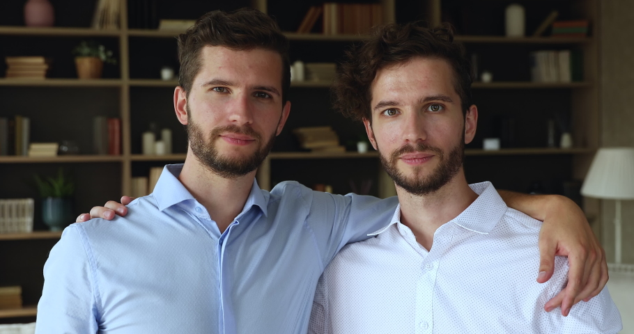 Head shot portrait friendly supportive millennial twin brothers stand close together hold hands on each other shoulders. Happy young males siblings twins hugging smiling looking at camera feel unity Royalty-Free Stock Footage #1087300115