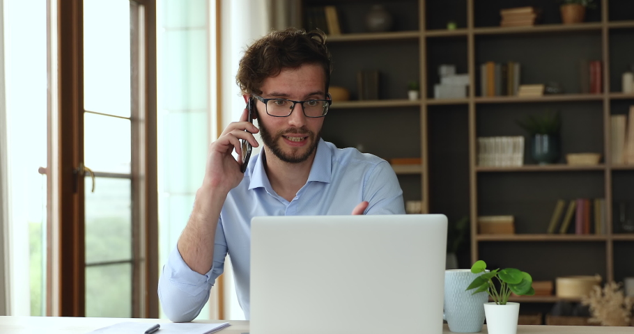 Busy millennial man office worker manager consulting client by telephone checking information on laptop screen. Professional teleworker broker salesman offer goods services remotely using phone laptop | Shutterstock HD Video #1087300121