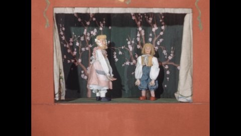 1940s: Boys look at paper and talk at desk in classroom. Curtains open on puppet theater. Marionettes walk onto stage and bow.