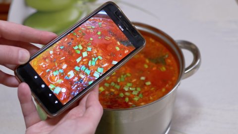 Female Hands are Recording a Video of Ukrainian Red Borscht on a Smartphone. Photographing food. Video, photo review of food through a mobile phone camera. Home kitchen. Fingerprints.