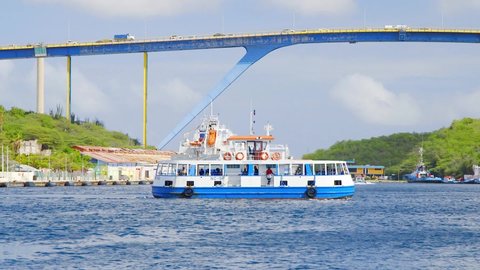 Willemstad , Curaçao - 01 05 2022: Tourist ferry crossing he famous Sint Anna Bay underneath the Queen Juliana Bridge in Willemstad