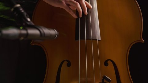 Male hands playing standup bass while recording with a microphone in foreground