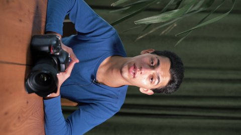 Video lesson on how to choose photographic equipment and how to work with it. A young attractive Muslim man is filming himself on camera. vertical video. Online tutor, mentor.