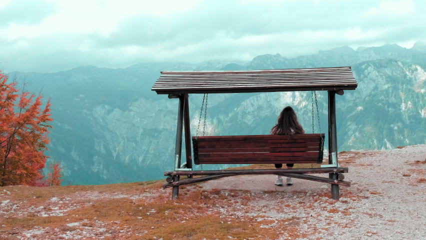 Woman swinging near lake Bohinj, Slovenia. Young woman sitting on hanging wooden swing enjoying mountain view and her travel vacation in autumn Alps. Handheld shot, back view. Royalty-Free Stock Footage #1087312556