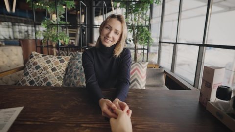 First-person view. The man gently holds the woman's hand. The beautiful blonde is not on a first date.