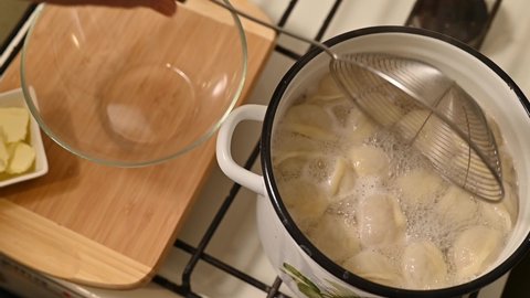 A woman prepares homemade meat dumplings. She takes the dumplings out of the boiling water and puts them in a transparent bowl.