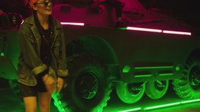 Group of stylish young people dancing , moving near military tank inside garage building Colorful stylish clothes , hippie style fashion . crazy  youth . Modern dances . Purple led light , slow motion