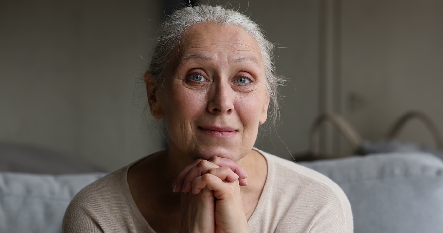 Close up kind older good-looking grey-haired woman sits on sofa looks into distance smiling while remembering past with warmth and gratitude. Carefree life of retiree on retirement, well-being concept Royalty-Free Stock Footage #1087319462