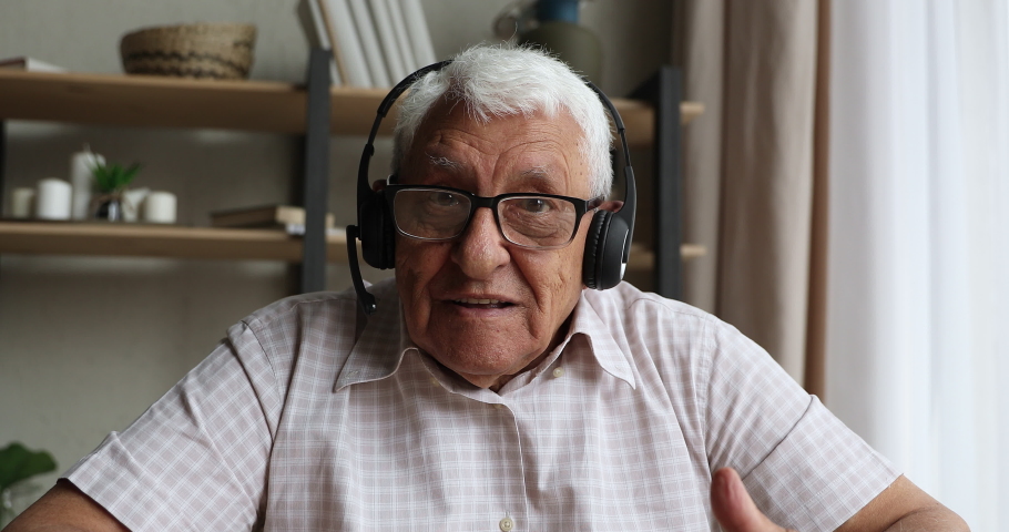Head shot portrait webcam view 70s man in headphones participates in video call virtual event. Tutoring on retirement, online medical consultation. Older generation use modern tech, videocall concept Royalty-Free Stock Footage #1087319525