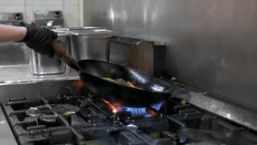Slow motion of Chef Cookin wokg in the Kitchen. Restaurant wok fire cooking Close up, cook frying vegetable in the commercial kitchen. High quality FullHD footage
