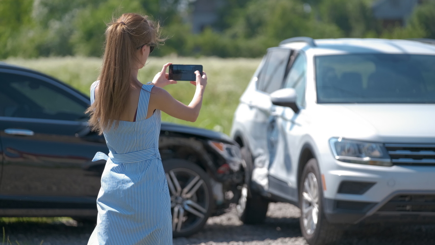 Stressed driver taking picture on sellphone camera of smashed vehicle calling for emergency service help after car accident. Road safety and insurance concept Royalty-Free Stock Footage #1087324325