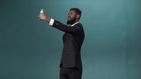 A handsome african man with a dark beard in a white shirt and black suit is making a video on his phone