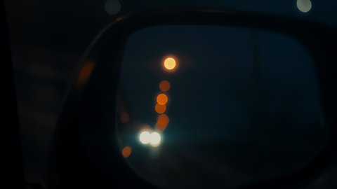 The side mirror of the car with bokeh highlights. A car driving through the night city. Bokeh road lights. Teal and Orange color correction.