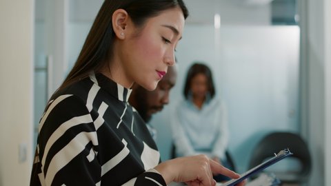 Asian woman looking at cv resume and preparing for job interview, waiting to start meeting about recruitment and selection. Candidate feeling nervous and reading files in queue.