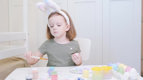 Little girl in Easter bunny ears painting eggs. Easter family holiday celebration at home. Child painting easter eggs. A 4-year-old girl with hare ears
