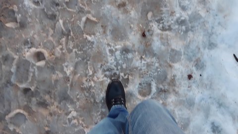Man walks along a road not cleared of dirty snow, slush in winter. First-person view of own feet. Above-zero temperature. Early spring after winter.