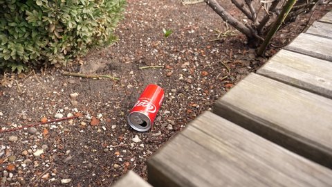 WROCLAW, POLAND - FEB 18, 2022: Garbage pollution - a coca cola can left as a trash on the ground near public place bench