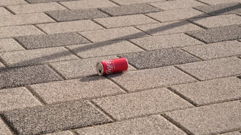 WROCLAW, POLAND - FEB 18, 2022: Garbage pollution - a coca cola can left as a trash on city sidewalk rolls over pavement on windy day