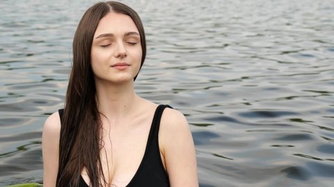 Portrait of a young cute girl with long hair on a background of water with waves. Slow motion portrait. Relax in nature. Summer rest