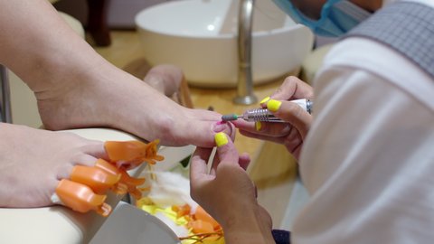 Beautician performs procedure, prepares and treats the client's nail with a liquid for removing old varnish from the fingers before the pedicure. Beautician removes old varnish with electrofreeze.