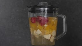 Blender with strawberries orange and apple making smoothie, close-up video