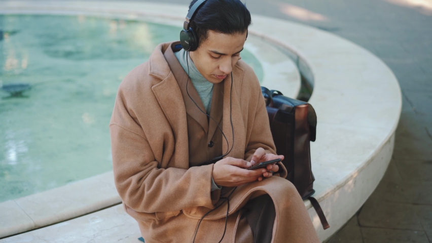 Overhead view of Arabian man texting by phone in headphones in the park