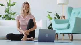 Young mother practicing yoga in front of device and having good time with daughter at home spbi. 4k video Attractive European female looks at computer screen with smile and does exercise, sits on
