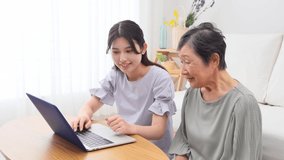 Asian grandchild and  her grandmother using the laptop at home
