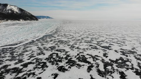Khivus or hovercraft rides on the ice of frozen Lake Baikal on a sunny winter day. There is snow near the shore, hummocks, blocks of ice. Winter trip .  Aerial view.