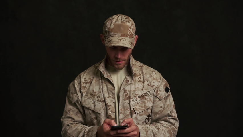 Angry military man texting by phone in black studio