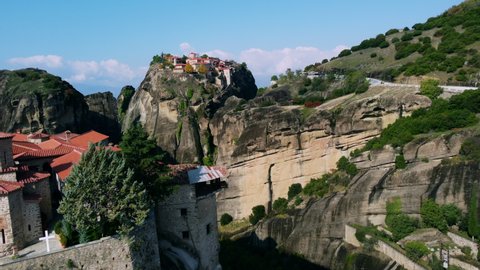 Drone flies between hills in Meteora Greece, where ancient two temples located at the summits. Bridge between two cliffs. Red roofs of the temples. Mountain landscape.